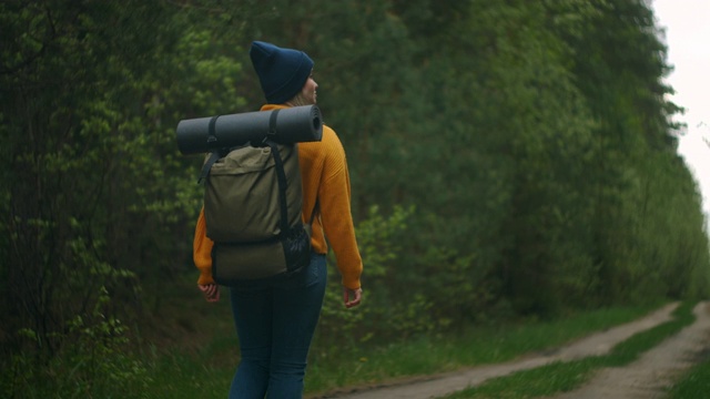 慢镜头:一名年轻女子在秋天的森林里徒步旅行。积极健康的白种女性背着背包，拿着木头。女性旅行者与徒步森林后视图，休闲，生物旅游，徒步旅行视频素材