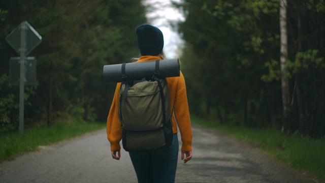 慢镜头:一名年轻女子在秋天的森林里徒步旅行。积极健康的白种女性背着背包，拿着木头。女性旅行者与徒步森林后视图，休闲，生物旅游，徒步旅行视频素材