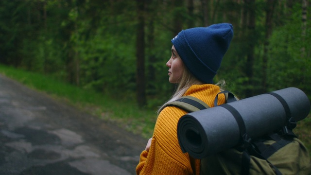 慢镜头:一名年轻女子在秋天的森林里徒步旅行。积极健康的白种女性背着背包，拿着木头。女性旅行者与徒步森林后视图，休闲，生物旅游，徒步旅行视频素材