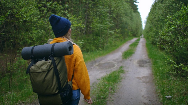 慢镜头:一名年轻女子在秋天的森林里徒步旅行。积极健康的白种女性背着背包，拿着木头。女性旅行者与徒步森林后视图，休闲，生物旅游，徒步旅行视频素材