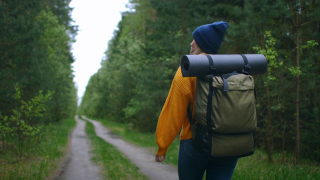 慢镜头:一名年轻女子在秋天的森林里徒步旅行。积极健康的白种女性背着背包，拿着木头。女性旅行者与徒步森林后视图，休闲，生物旅游，徒步旅行视频素材