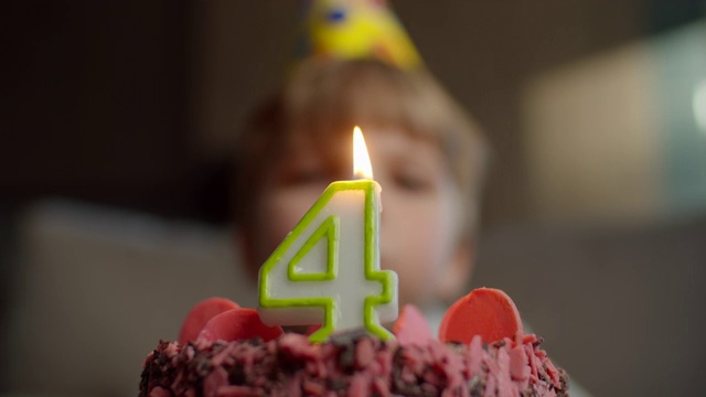 小朋友吹灭巧克力生日蛋糕上的4号蜡烛的特写。4岁的男孩庆祝生日。视频素材