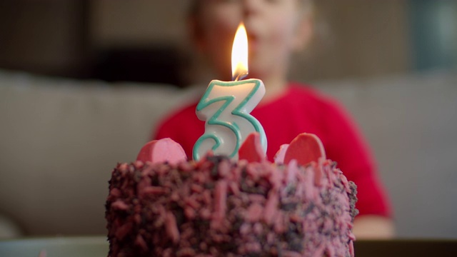 孩子吹灭巧克力生日蛋糕上的3号蜡烛的特写。三岁的女孩庆祝生日。视频素材