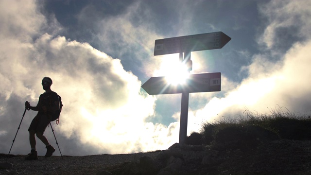 十字路口的徒步者拿着背包、靴子和登山杖，举着路标走过来。云在背景上移动。视频素材