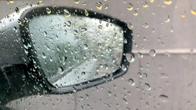 雨点落在车窗上。透过带有雨滴的车窗看到的汽车后视镜。4 k。视频素材