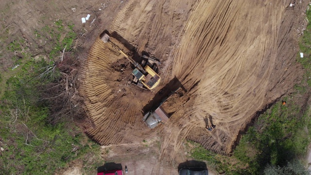 鸟瞰图:黄色挖掘机将土倒入自卸车。准备地方建设住宅。4 k视频素材