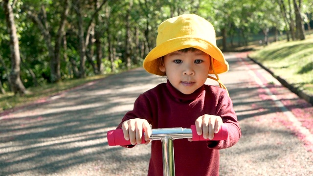 一个快乐的小女孩骑着滑板车在夏季公园的路上。幸福家庭和童年的概念。视频素材