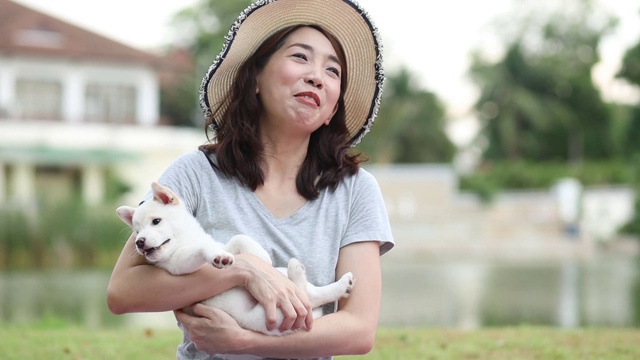 宠物情人。亚洲妇女抱着白色柴犬或北海道犬在公园里。夏天，妈妈和柴犬在公园里玩耍。视频素材