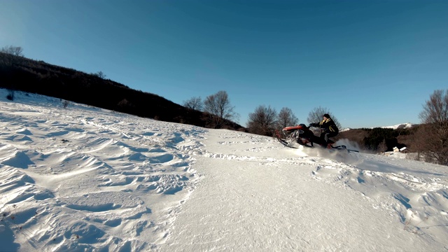 在蓝天的背景下，一个家伙骑着雪地摩托飞行，留下一串白色的雪花飞溅的慢镜头。明亮的雪地摩托和西装没有品牌视频素材