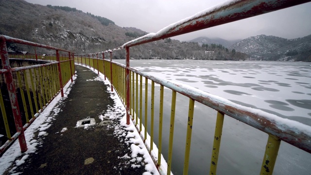 从结冰的湖和积雪的森林的桥上看到的美丽的冬季景观视频素材