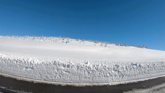 驾驶POV的一条积雪的山路，山上覆盖着积雪和常青树视频素材