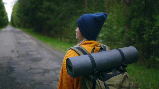 一位穿着黄色毛衣、背着背包的女性旅行者正走在森林里的一条小路上，欣赏着美丽的景色。女性旅行者探索森林在毛衣和背包视频素材