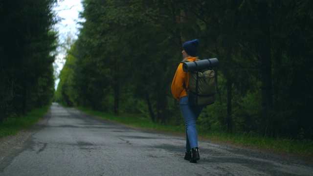 一位穿着黄色毛衣、背着背包的女性旅行者正走在森林里的一条小路上，欣赏着美丽的景色。女性旅行者探索森林在毛衣和背包视频素材