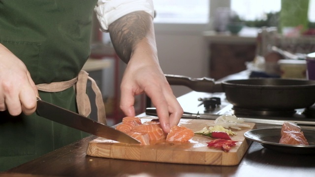 男厨师将新鲜的鲑鱼片切成大块。在厨房做鱼。由厨师准备食材来制作菜肴。在餐厅厨房做饭。美食家的食物配料视频素材