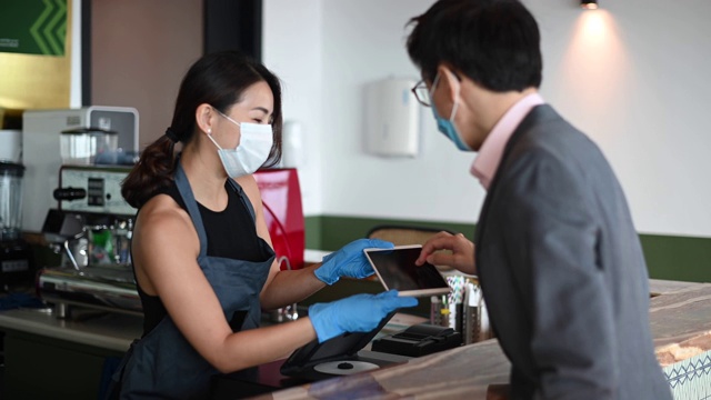 一位亚洲华裔女店主在柜台用数码平板电脑为她的顾客点菜视频素材