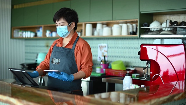 一个亚洲的中国小企业主戴着口罩和防护手套在结账时输入视频素材