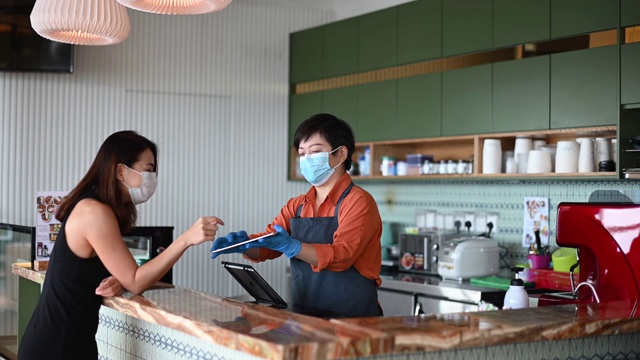 一位亚洲华裔女店主在柜台用数码平板电脑为她的顾客点菜视频素材