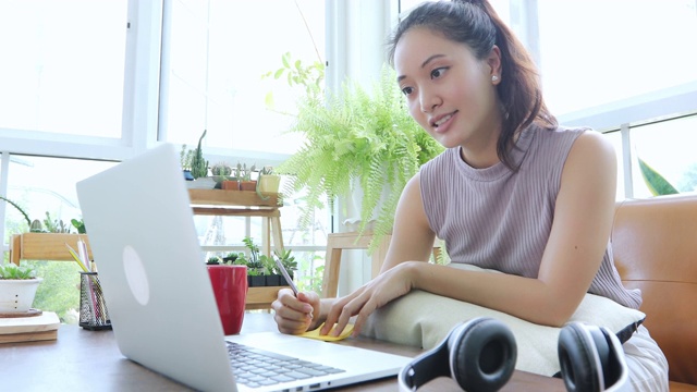 亚洲的商业女性使用笔记本电脑，在网上开会和在家工作时戴着耳机。视频素材