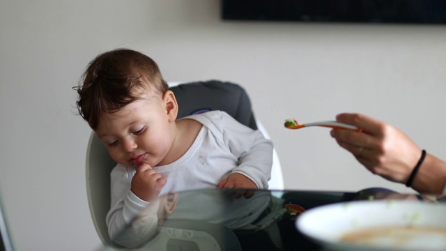 蹒跚学步的婴儿拒绝喂食，一岁的婴儿坐在高脚椅上拒绝进食视频素材