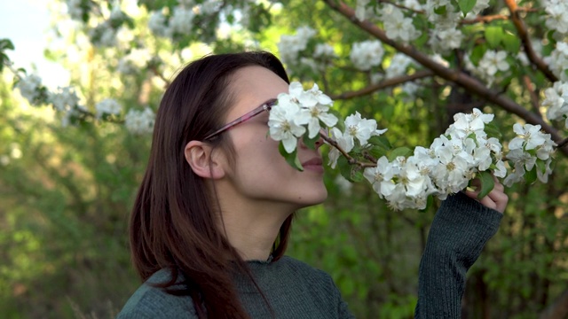 一个年轻女子在闻一棵开花的树。苹果园里的女孩。特写镜头视频素材