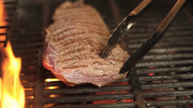 厨师用钳子把一块多汁的生肉放在火上的热烤架上。视频素材