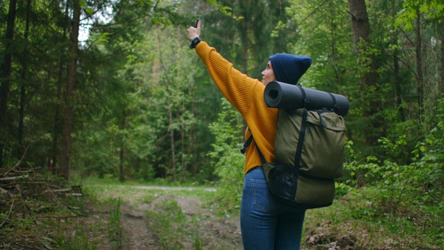 慢镜头:一名年轻女子在森林里用智能手机享受周末。旅行的女人背着背包走在森林的小路上，在绿色的树林里看电话和地图视频素材