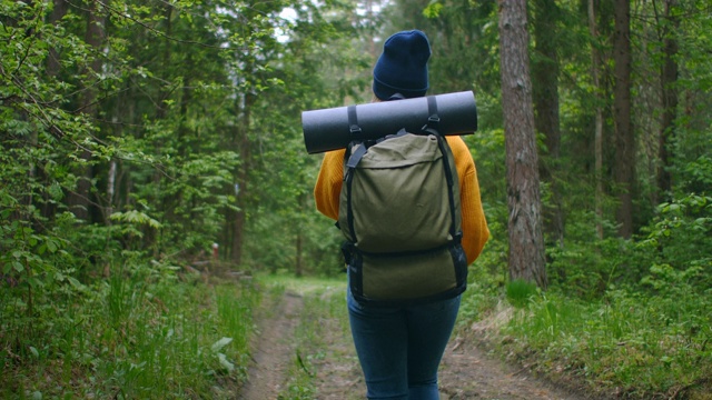 慢镜头:一名年轻女子在森林里用智能手机享受周末。旅行的女人背着背包走在森林的小路上，在绿色的树林里看电话和地图视频素材