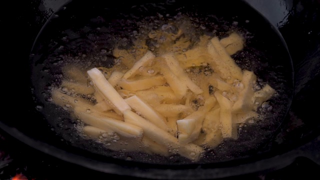 用滚烫的油在平底锅里炸土豆条。切片土豆在油煮沸特写。慢慢地视频素材