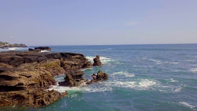 无人机在蓝色海洋上空飞行，海岸边有巨大的石阵视频素材