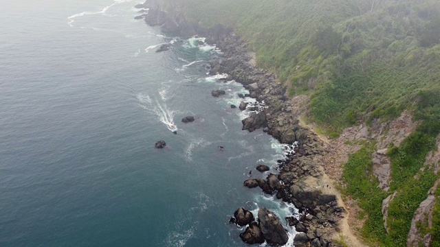 无人机拍摄到沿多岩石海岸线行驶的摩托艇视频素材