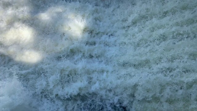 在阳光明媚的天气里，湍急的水流在森林里的小河上的一个小水坝上流动视频素材