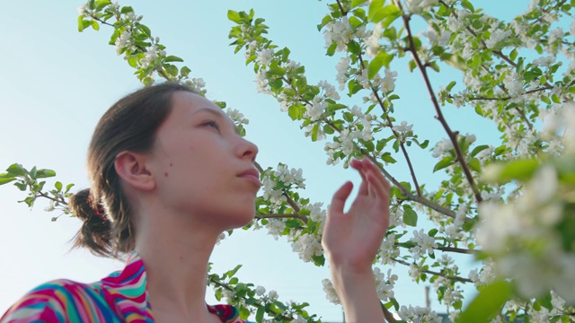 美丽的亚洲女孩正在闻树上的花。樱花或苹果树，粉红色的花，叶子。绿意盎然，春意盎然。日本风格的微笑女子肖像视频素材