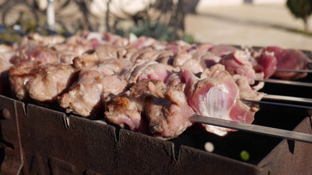 外面的火盆上烤着牛肉串。特写的羊肉串在户外的明火上烧烤。在后院的晚餐聚会上，用金属串烤猪肉。视频素材