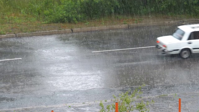 沥青路上下着大雨。旧汽车在雨点间的道路上行驶视频素材