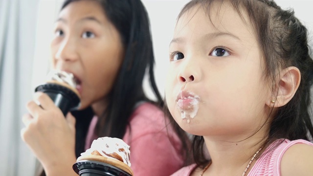 亚洲小孩和她妹妹在家里吃蛋筒冰淇淋，慢镜头。视频素材