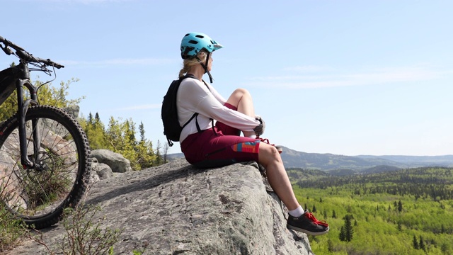 女山地自行车骑手在山杨树上的悬崖顶上放松视频素材