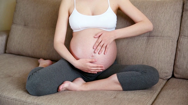 一个孕妇在沙发上抚摸她的肚子的特写视频素材