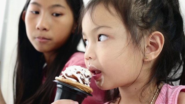 亚洲小孩和她妹妹在家里吃蛋筒冰淇淋，慢镜头。视频素材