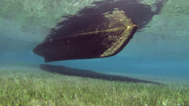 浅水区的渔船站在覆盖着绿色海草的海床上，沐浴着阳光。水下视图视频素材