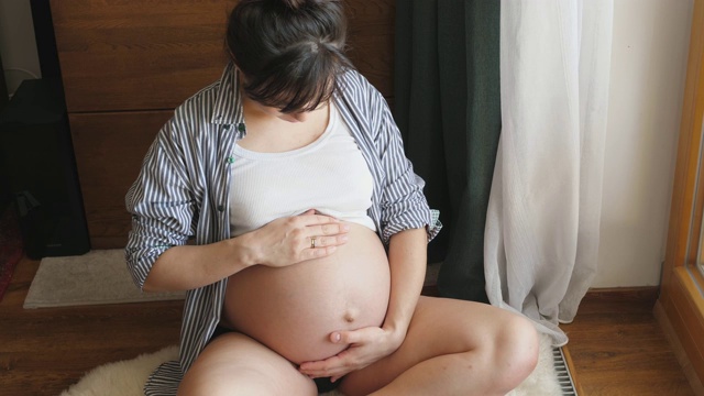 孕妇坐在地板上等待母亲抱着怀孕的肚子里的婴儿视频素材