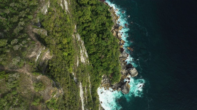 从上面俯瞰，令人惊叹的鸟瞰图，岩石嶙峋的海岸线沐浴在汹涌的大海中。努沙佩尼达，巴厘岛，印度尼西亚。视频素材