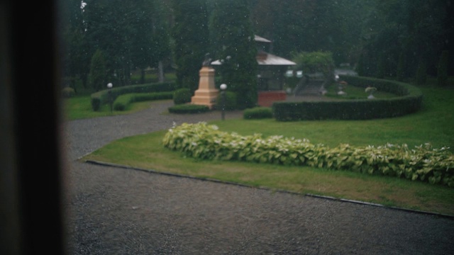 慢镜头雨点落在窗外绿树成荫的玻璃窗上。视频素材