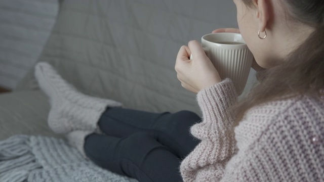 女孩穿着暖和的衣服，喝着茶。视频素材