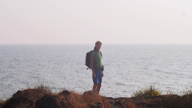 背景肖像旅游背包客站在海洋背景拷贝空间。徒步旅行者看着蓝色的水面独自缓慢移动。旅游旅游，暑假探险视频素材