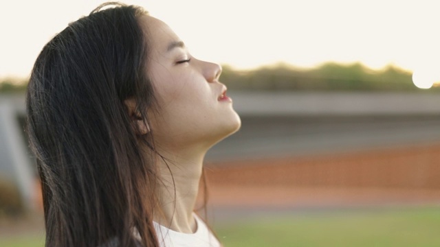 年轻的亚洲女孩的近距离肖像放松享受和平的日落，抬头呼气新鲜空气放松在一个公园在美丽的夏季日落。视频素材