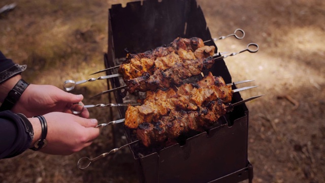 男手在户外烧烤肉。野餐时用木炭烧烤肉。视频下载