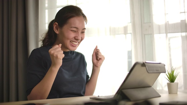 慢镜头亚洲女人在家里用笔记本电脑庆祝我的成功视频素材