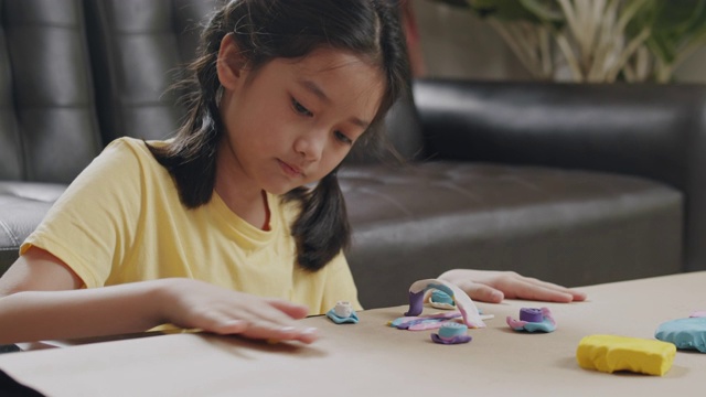 亚洲小女孩呆在家里的时候，在客厅里玩塑泥和制作工艺品。她在桌子上用自己的想象塑造五彩的橡皮泥创作艺术作品。艺术和工艺概念。视频素材