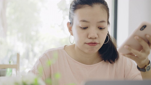 亚洲商务女性在家工作，桌上放着智能手机和笔记本电脑，心情愉快。社会距离的概念，以阻止冠状病毒疾病的传播。4 k UHD。缓慢的运动。视频素材