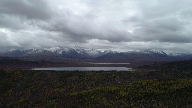 美丽的大森林在地平线，雪山，石峰。高全景飞无人在农村植物。旅游目的地田园风光。傍晚烟雾戏剧性的天空和宁静的池塘宽拍摄视频素材